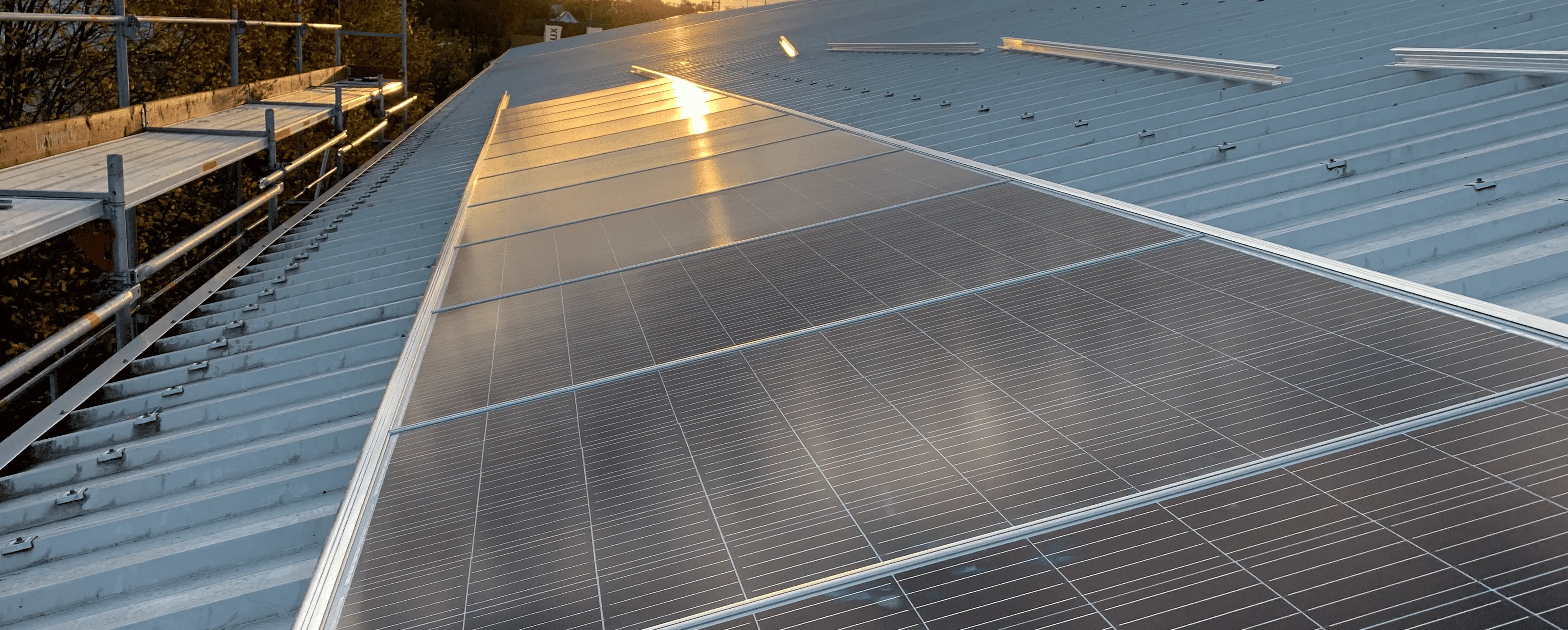 Solarpanel-Reihe auf einem blauen Metallblechdach mit Sonnenlichtreflexion bei Sonnenuntergang.