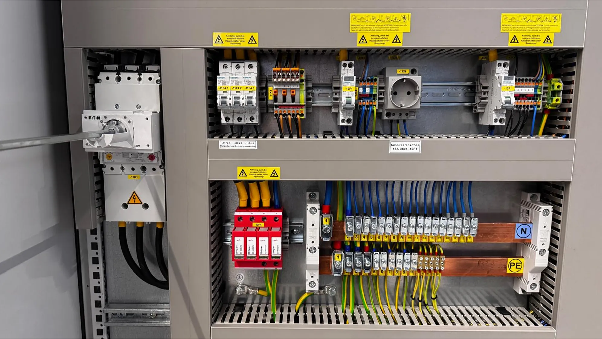 Elektrischer Schaltschrank mit mehreren Sicherungen, Steckdose und geordneten Kabeln in verschiedenen Farben.
