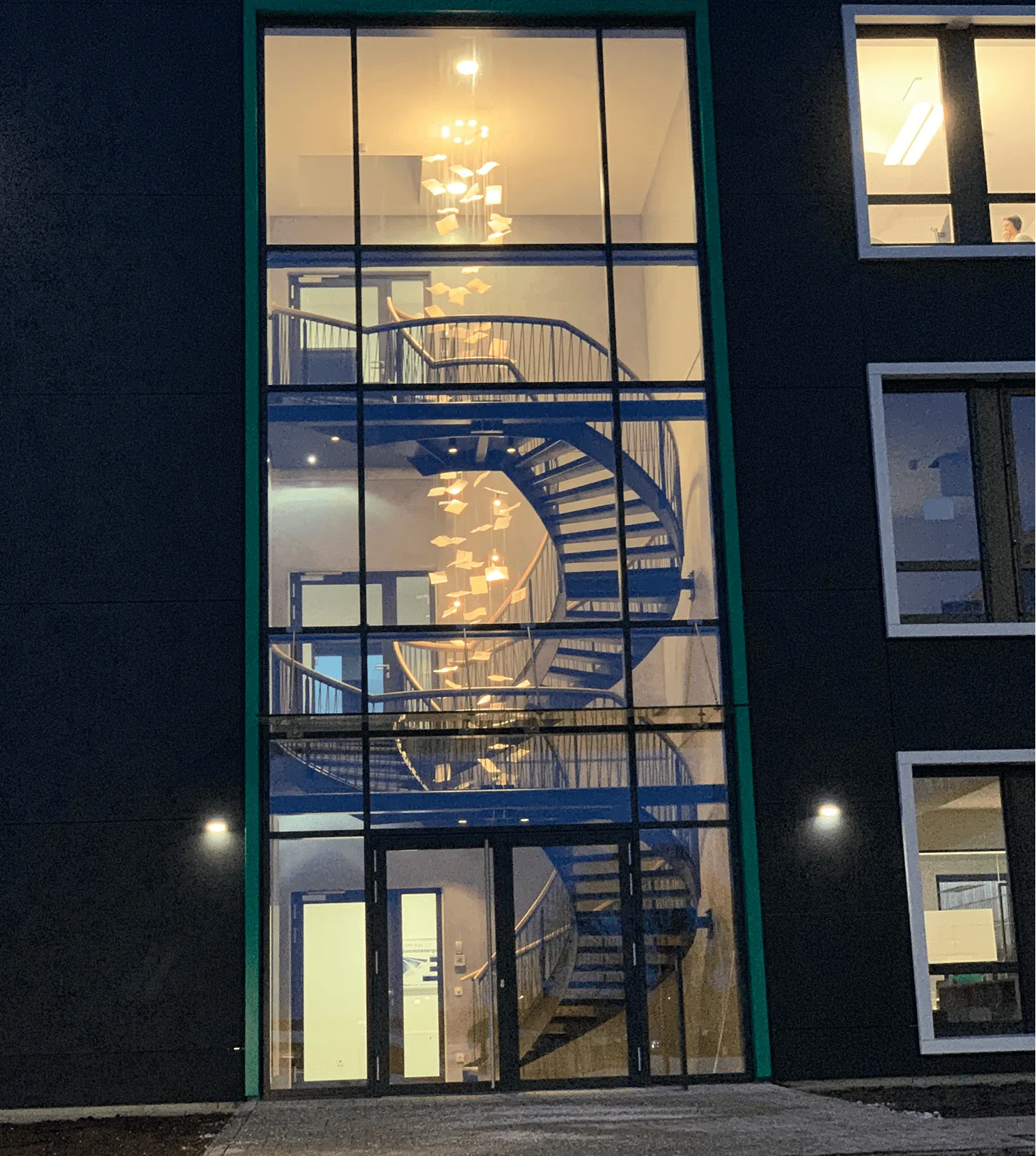 Beleuchtetes Treppenhaus mit spiralförmiger Treppe und hängender Dekoration aus Papierbögen bei Nacht.